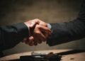 Two people shaking hands over a table, representing a partnered Bitcoin mining arrangement split automatically through ViaBTC Revenue Sharing